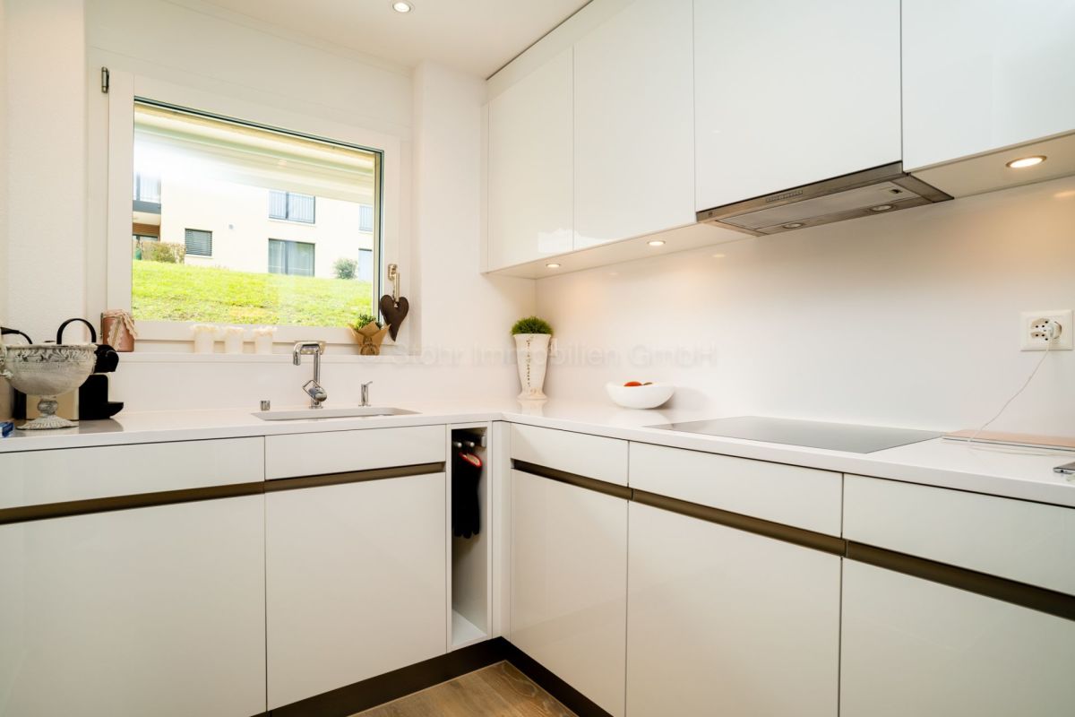 Moderne weiße Einbauküche mit Fensterblick ins Grüne