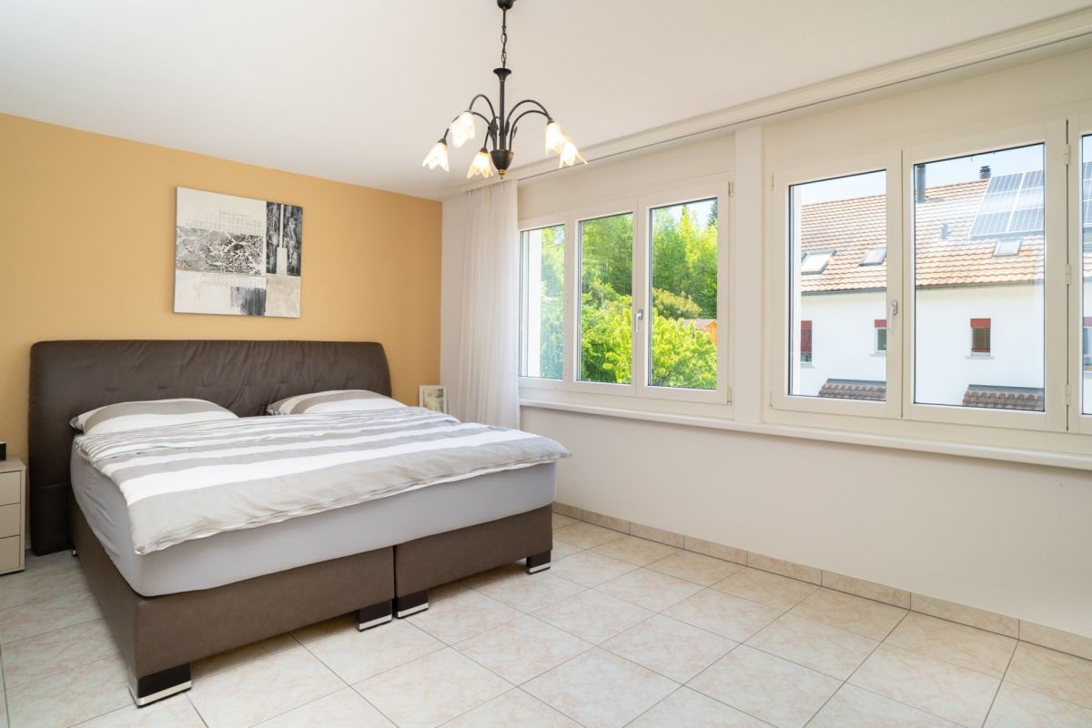 Helles Schlafzimmer mit Fliesenboden und großen Fenstern