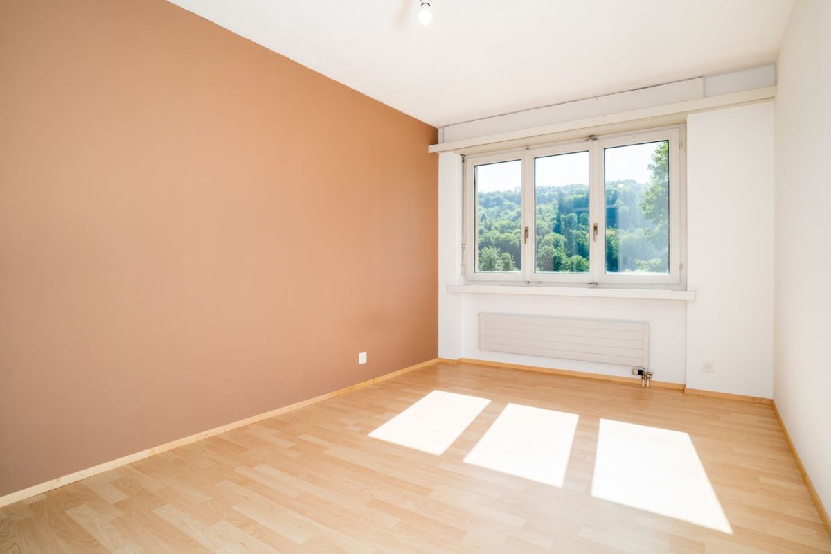 Helles leeres Zimmer mit Holzoptik-Boden und Blick ins Grüne