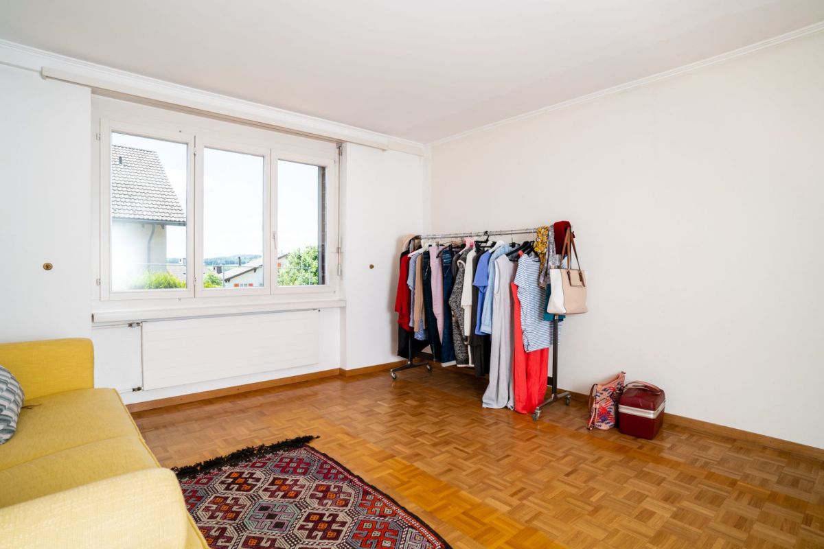 Helles, leer wirkendes Zimmer mit Fenster, Sofa und Kleiderständer