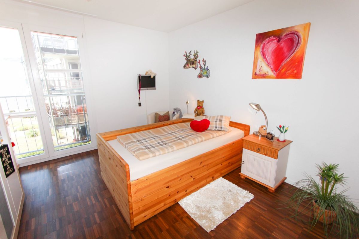 Helles Schlafzimmer mit Holzbett und Balkonfenstern