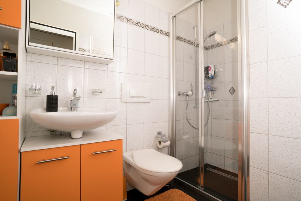 Modernes kleines Badezimmer mit Dusche und orangefarbenem Waschtischunterschrank