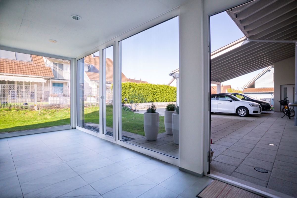 Verglaster Innenraum mit Blick in den Garten und zur überdachten Einfahrt