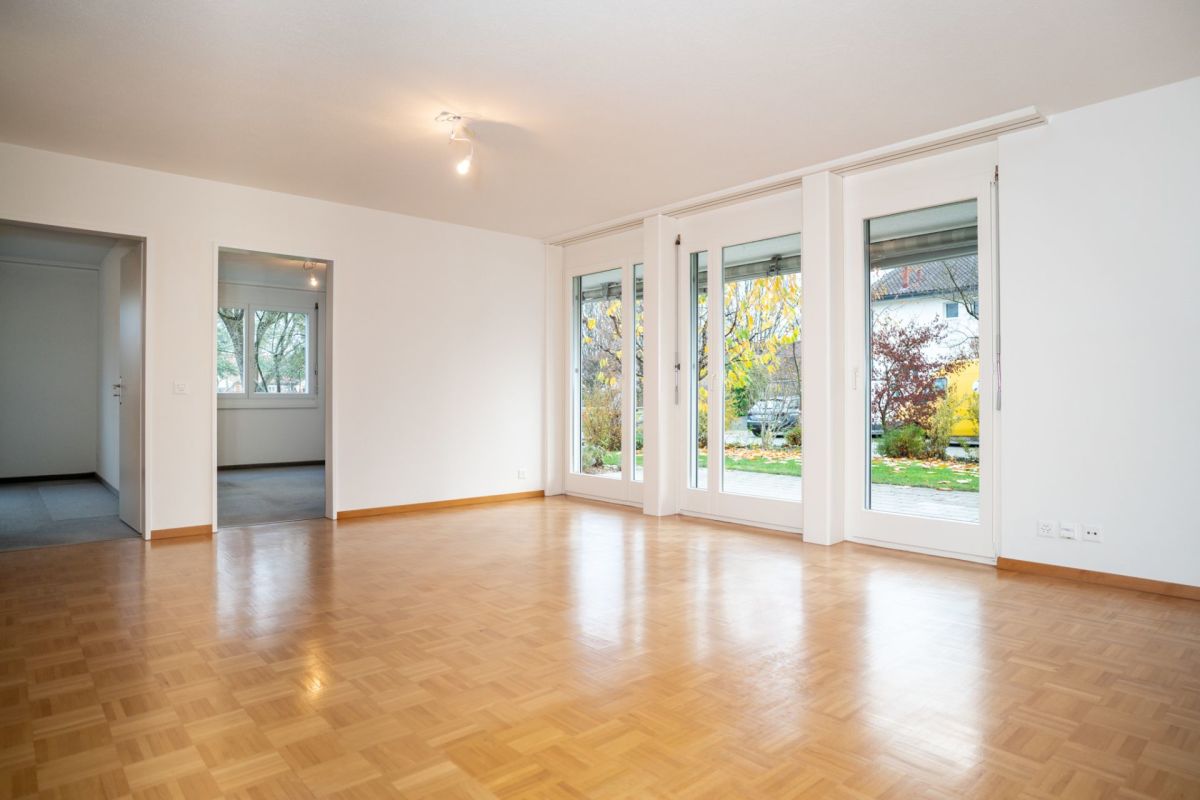 Heller leerer Wohnraum mit Parkettboden und großen Fenstertüren