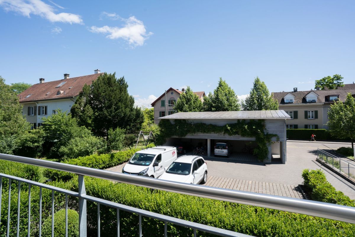 Blick von einem Balkon auf eine ruhige Wohnanlage mit Carport und viel Grün