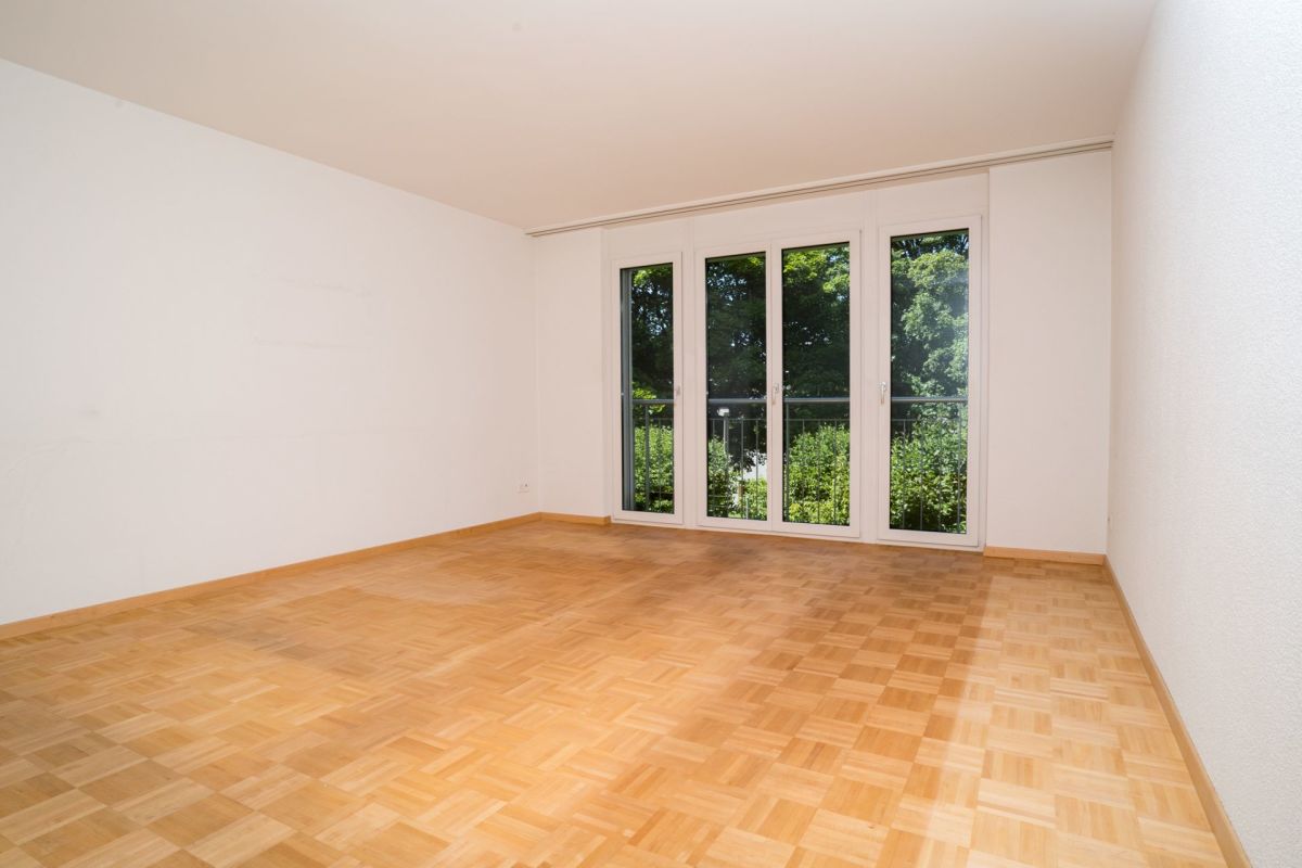Heller leerer Wohnraum mit Parkett und Balkonfenstern