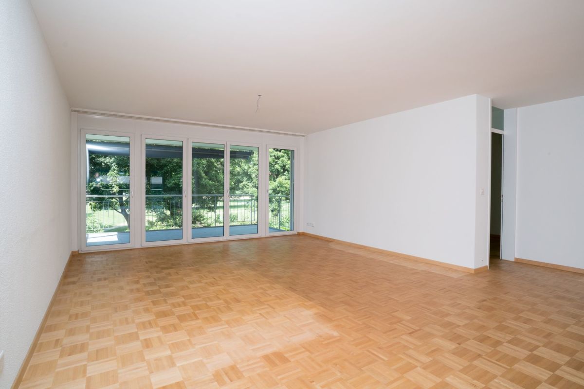 Leerer Wohnraum mit Parkett und großer Fensterfront