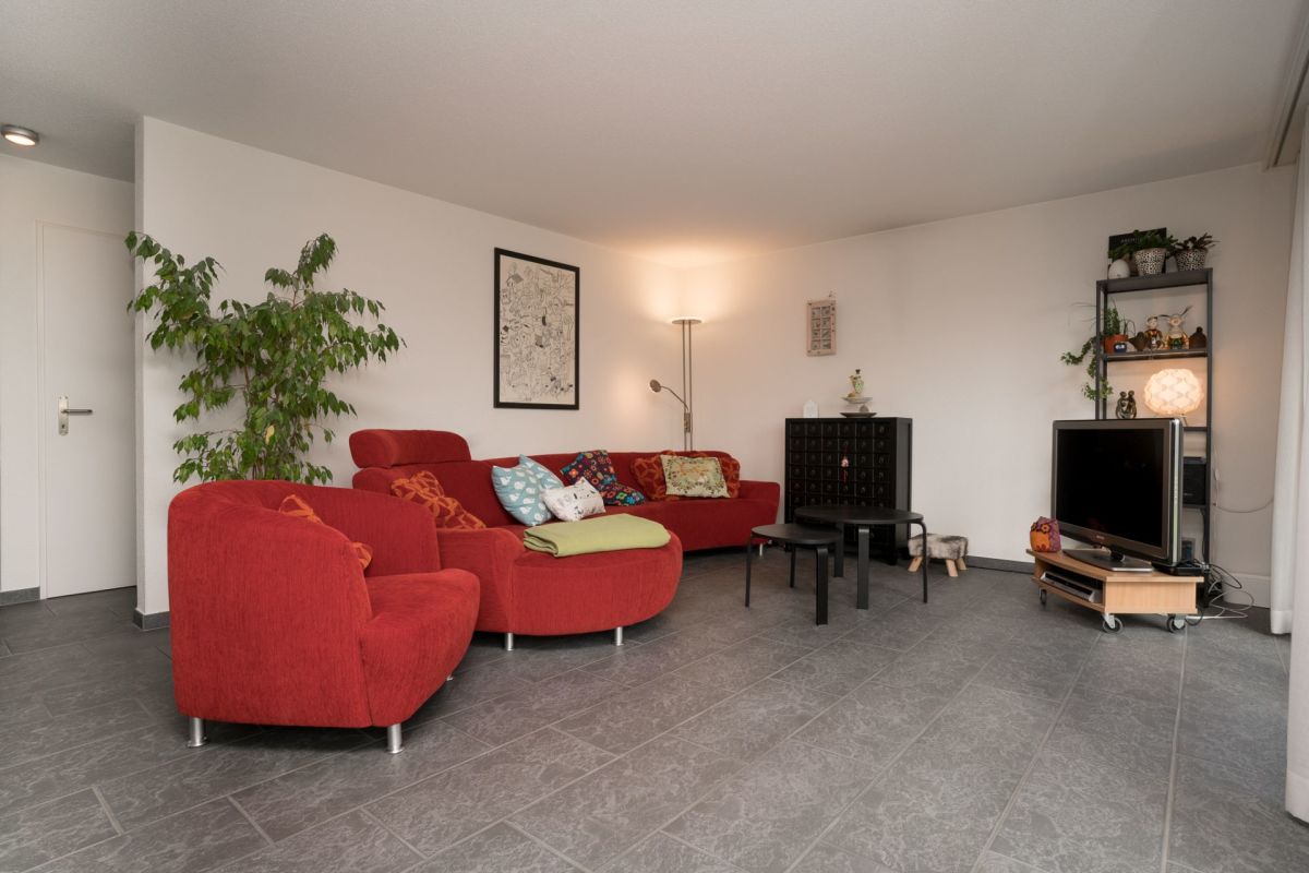 Wohnzimmer mit rotem Sofa und grauem Fliesenboden