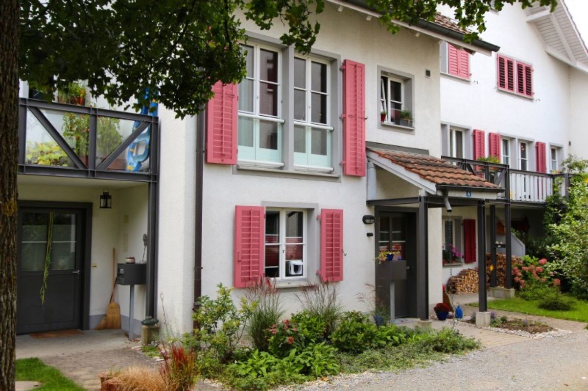 Mehrfamilienhaus mit rosafarbenen Fensterläden und Garten