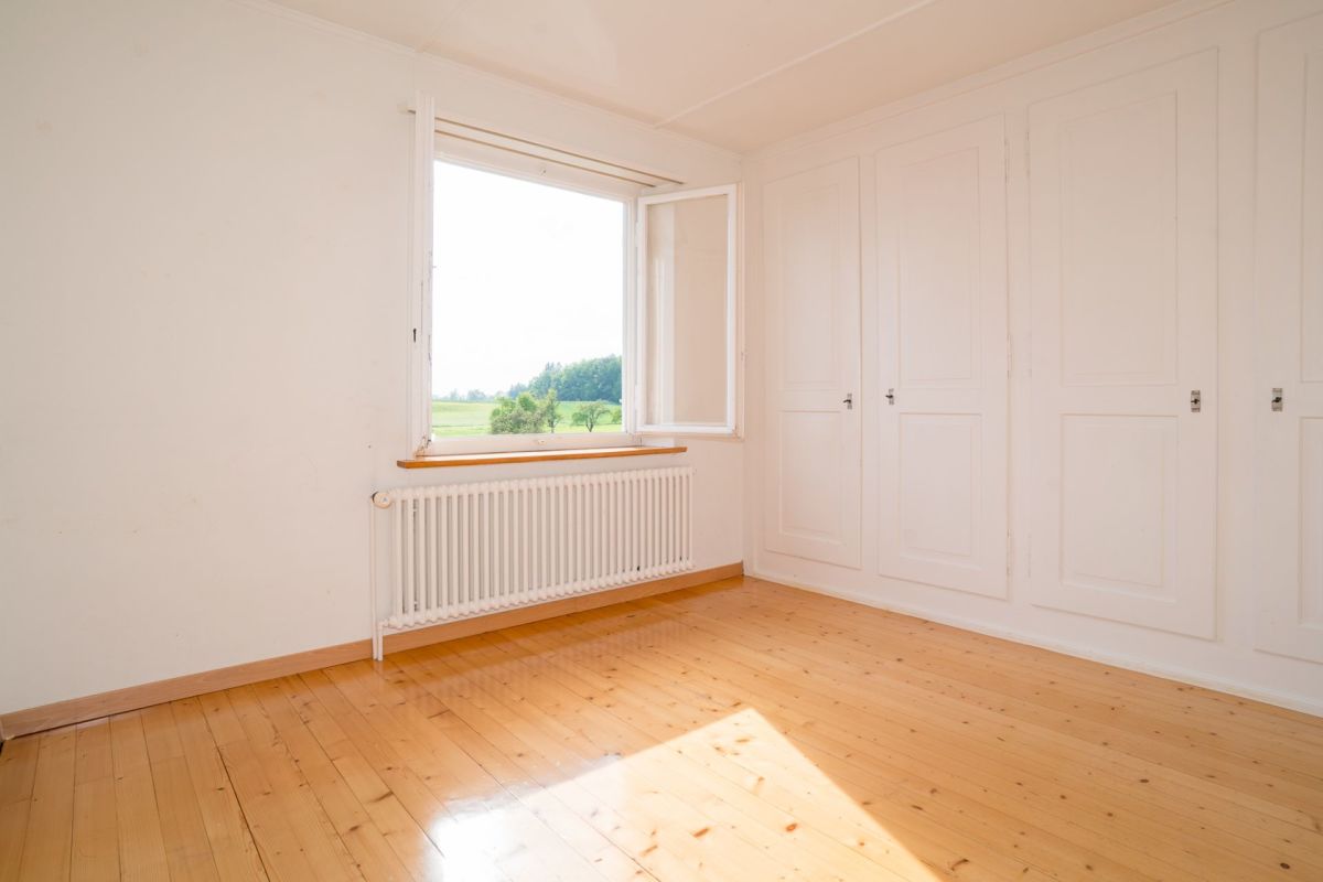 Helles, leeres Schlafzimmer mit Holzboden und offenem Fenster