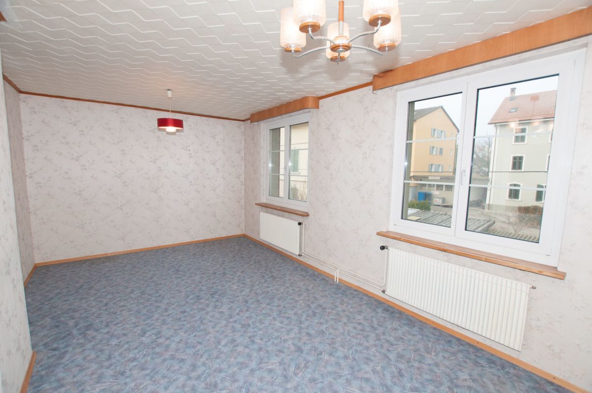Leeres Wohnzimmer mit Teppichboden und großen Fenstern
