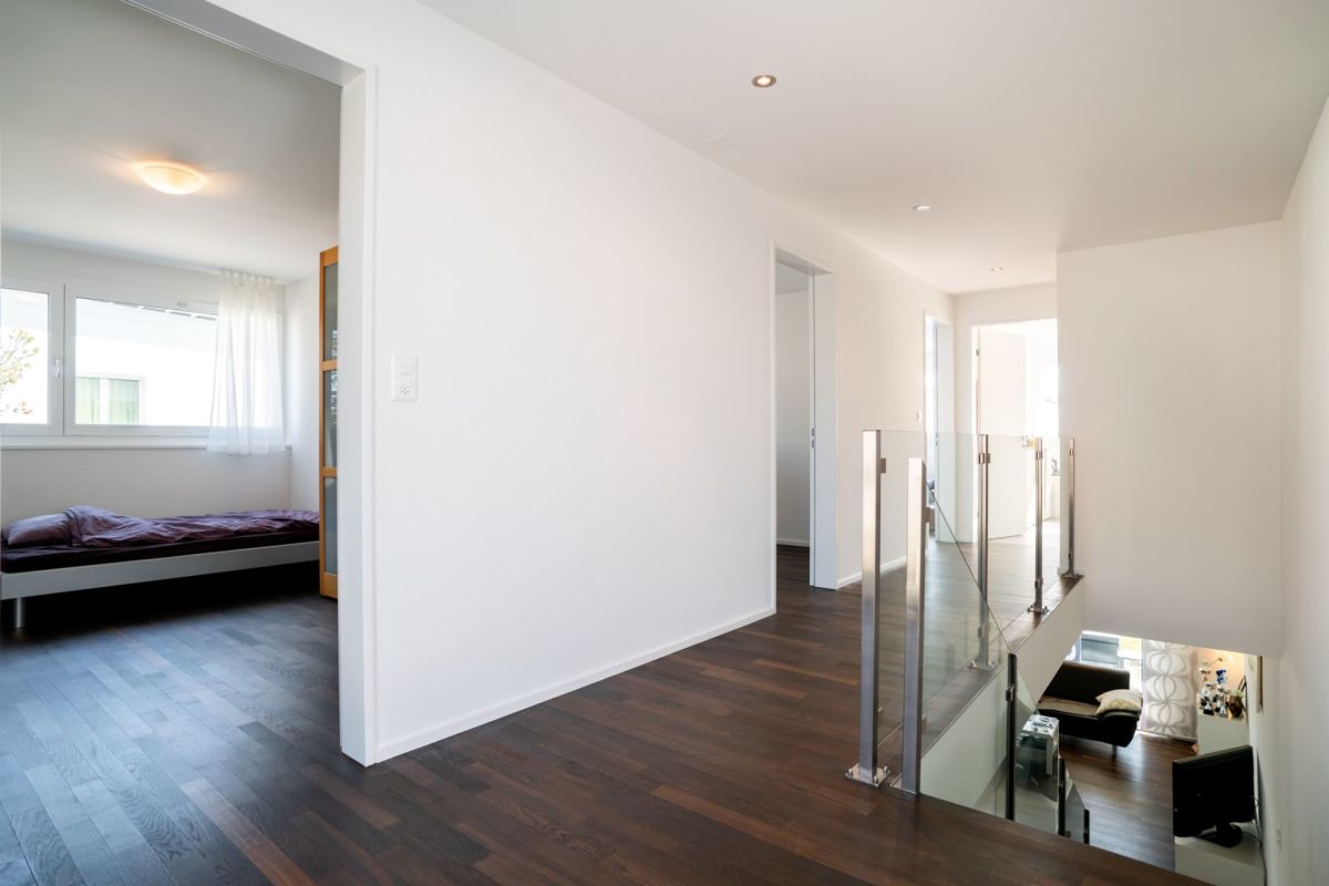 Heller Flur mit Blick in ein Schlafzimmer und auf eine Galerie mit Glasgeländer.