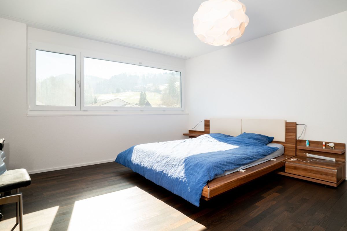 Helles Schlafzimmer mit großem Fenster und Holzbett