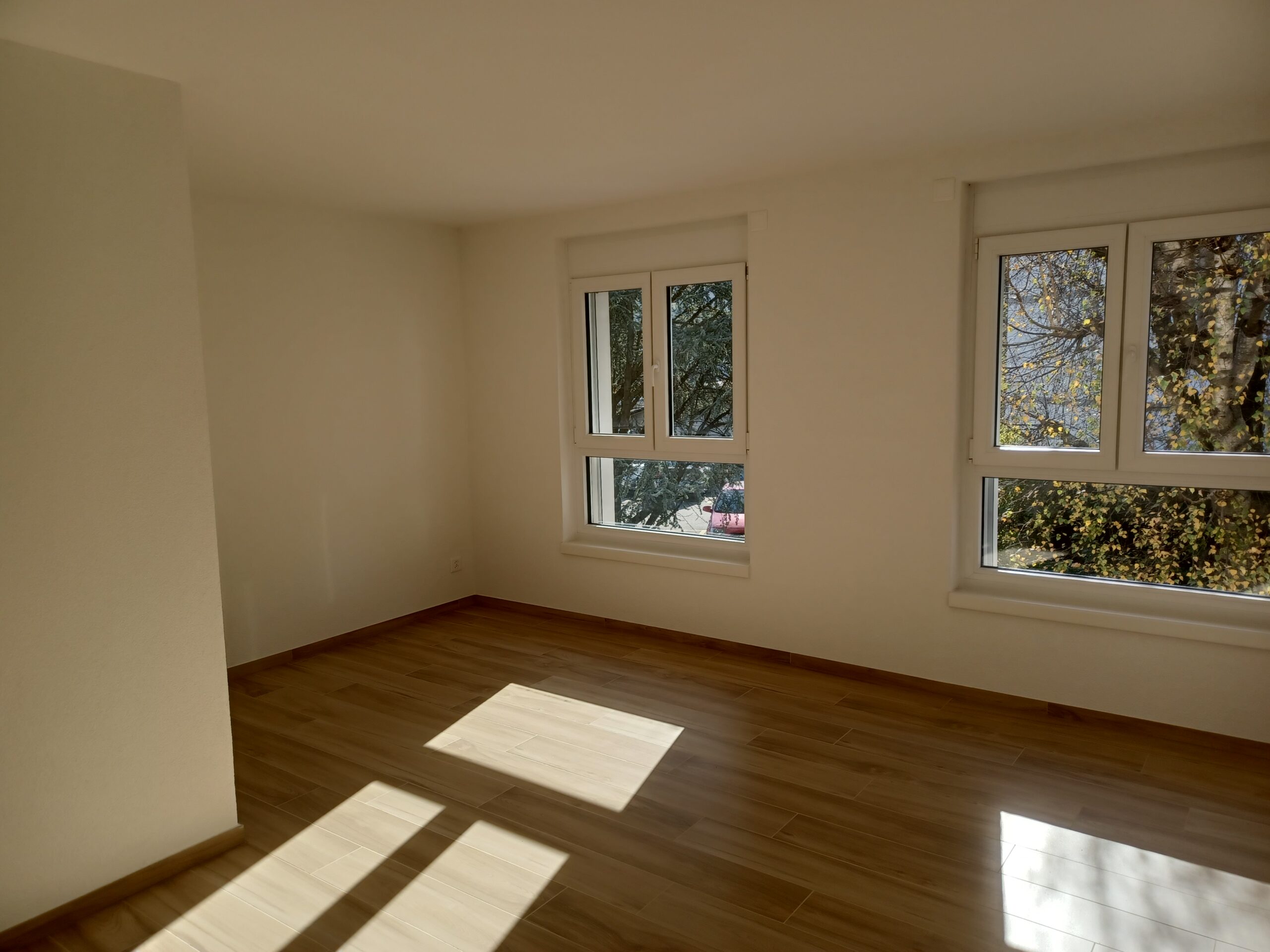 Heller leerer Raum mit zwei Fenstern und Holzoptikboden