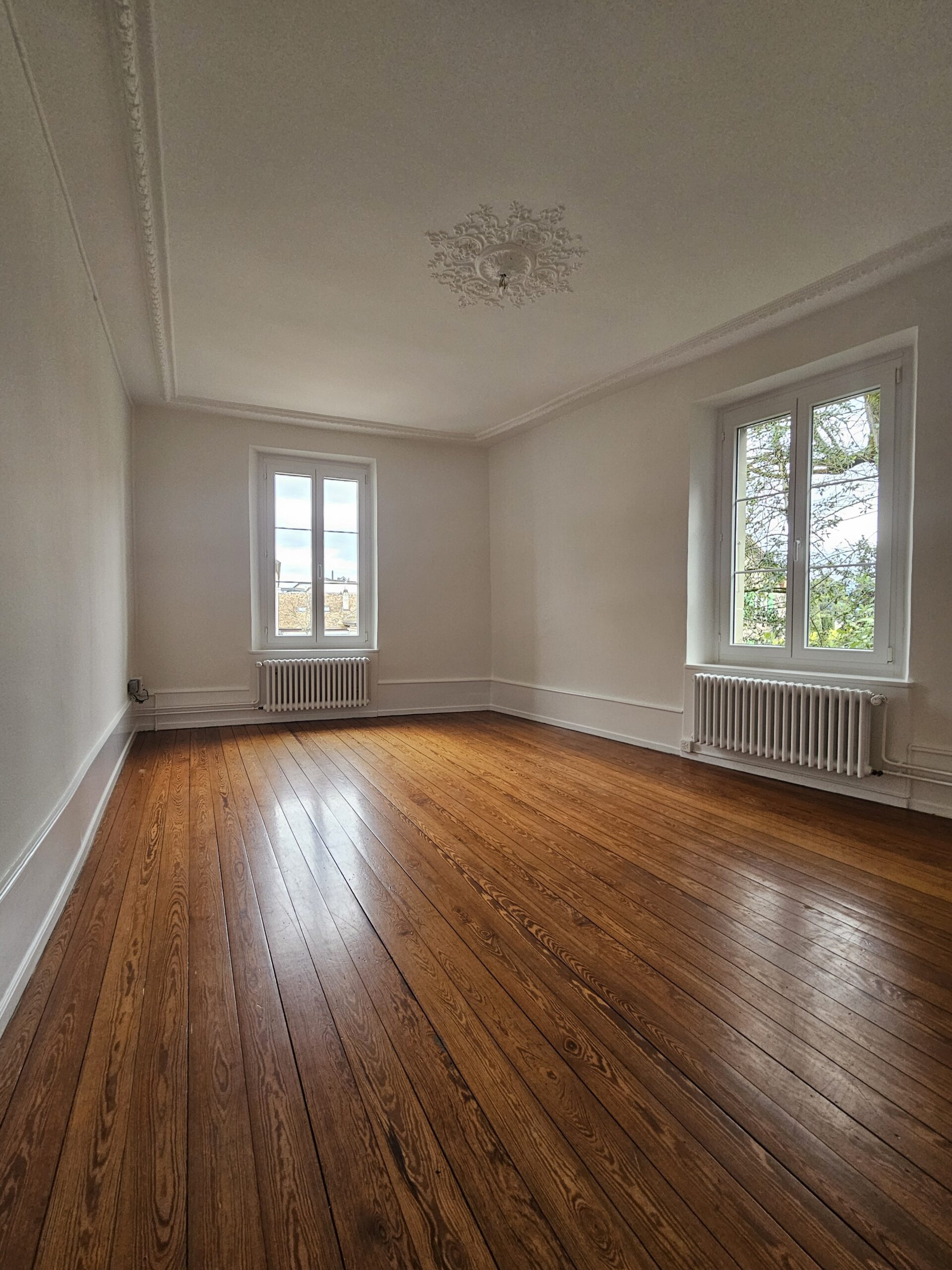 Leerer Altbau-Raum mit Holzparkett und Stuckdecke