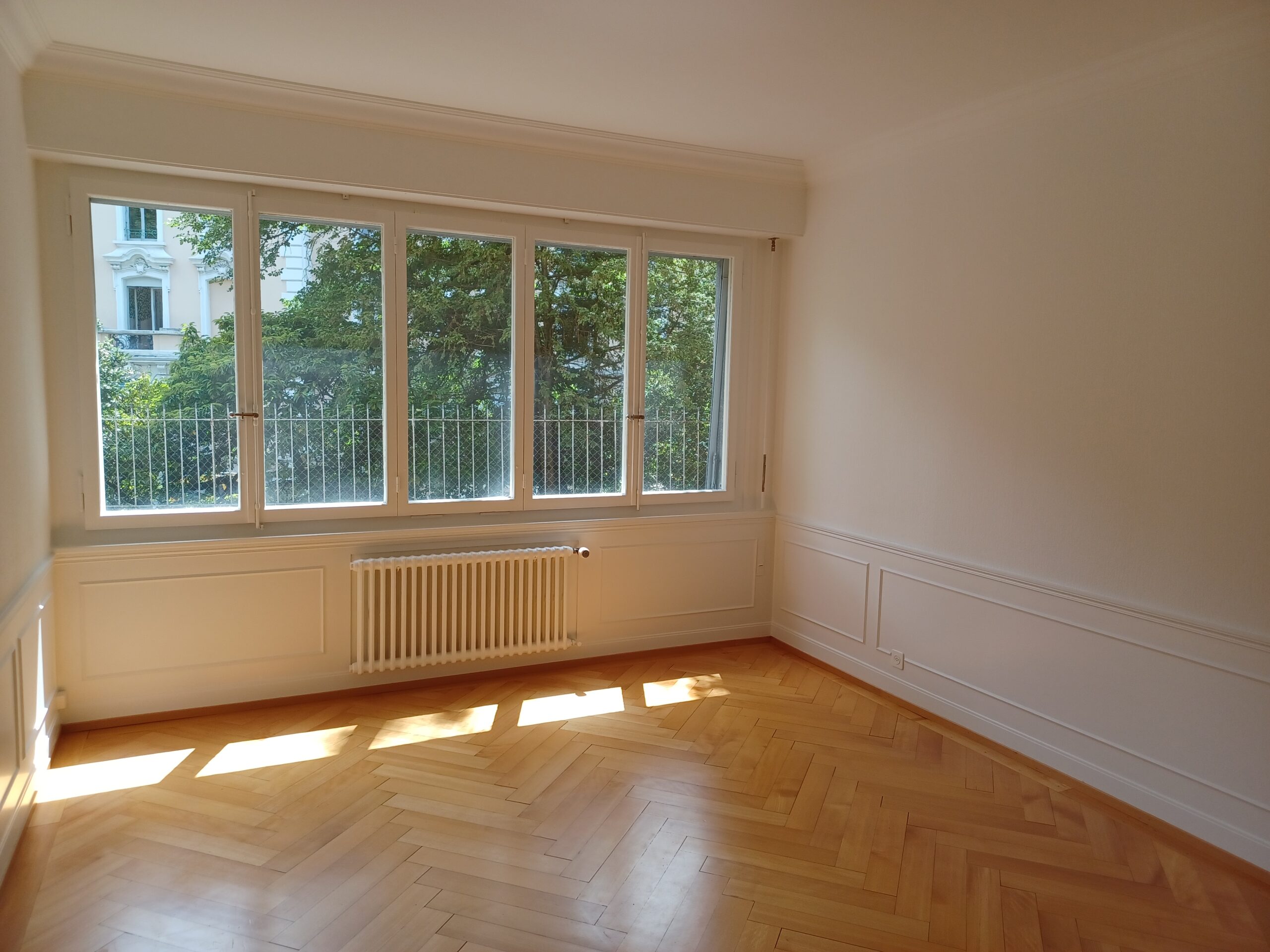 Heller leerer Raum mit großem Fenster und Fischgrätparkett