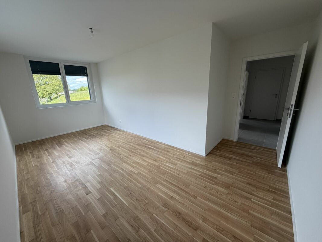 Helles, leeres Schlafzimmer mit Laminatboden und Fensterblick ins Grüne