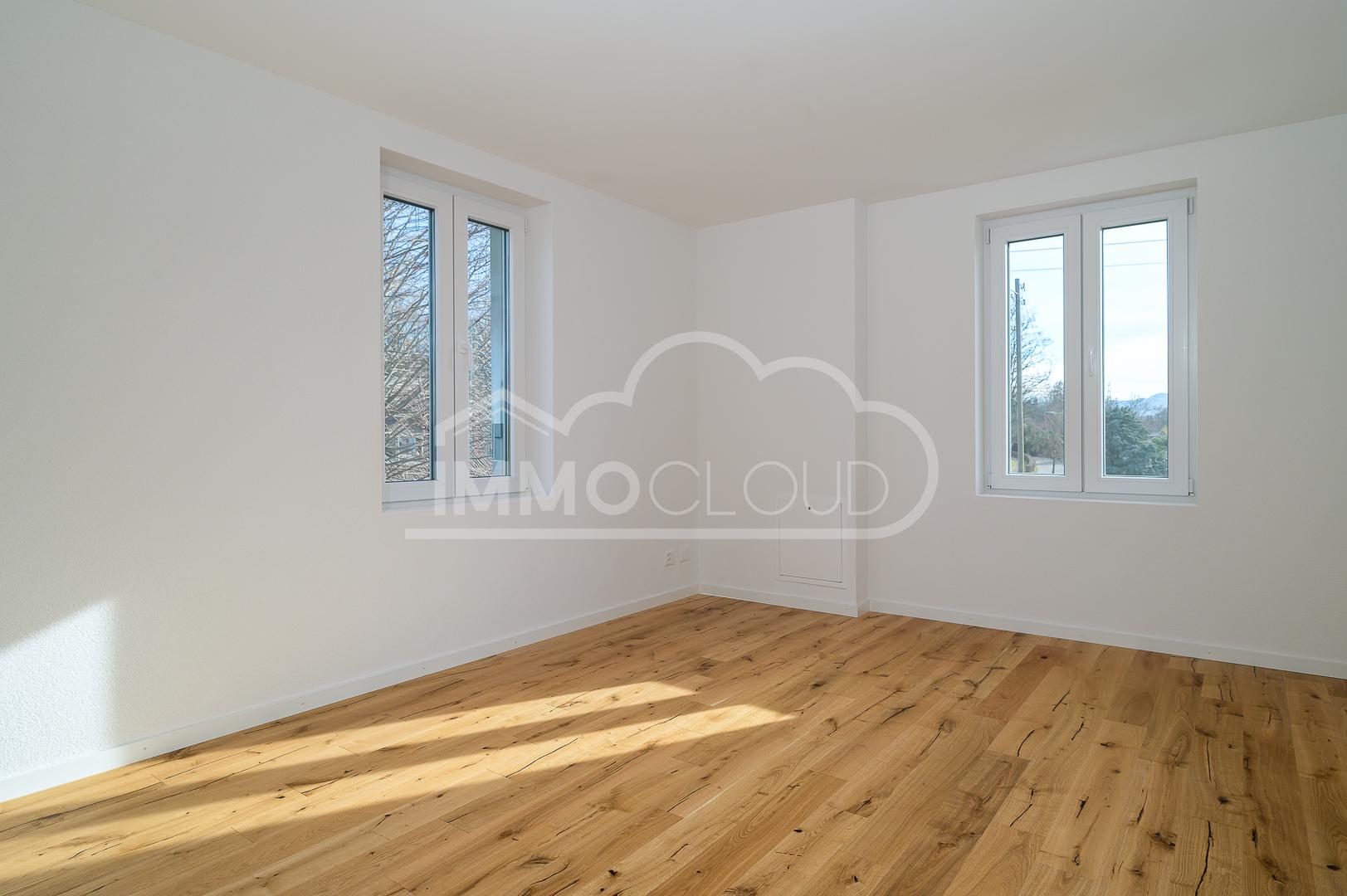 Helles, leerstehendes Zimmer mit Holzfußboden und zwei Fenstern