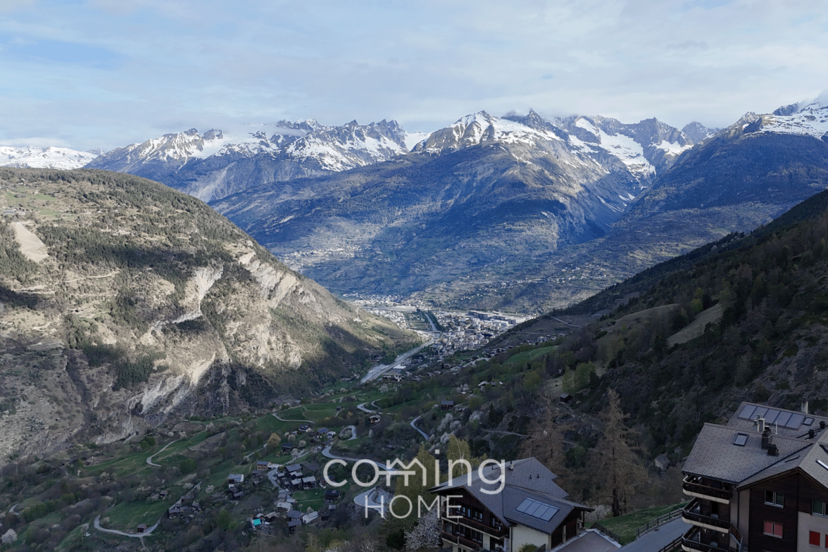Alpenpanorama über ein Tal mit Bergdorf und Schneegipfeln