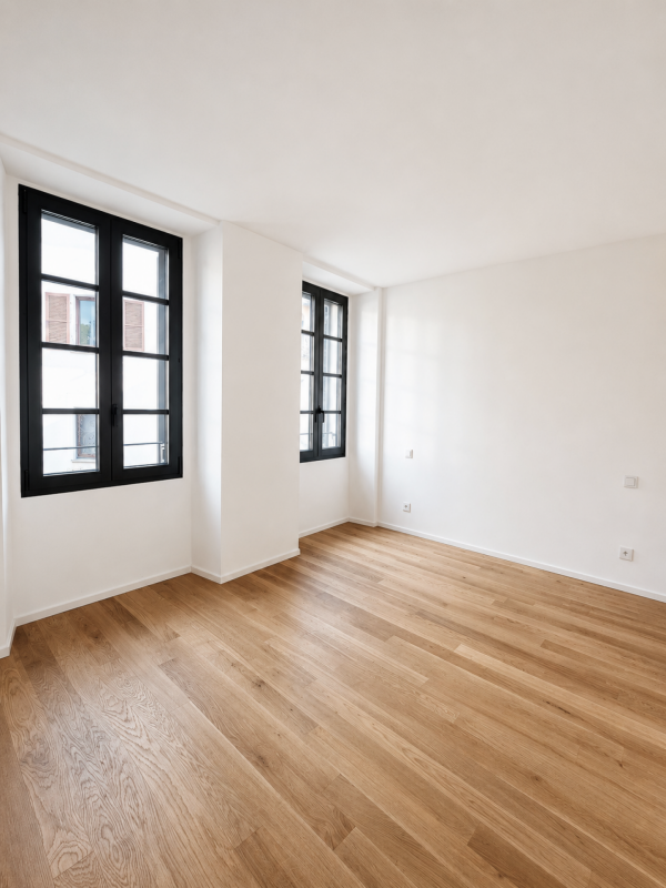 Heller leerer Raum mit Holzboden und schwarzen Fenstern