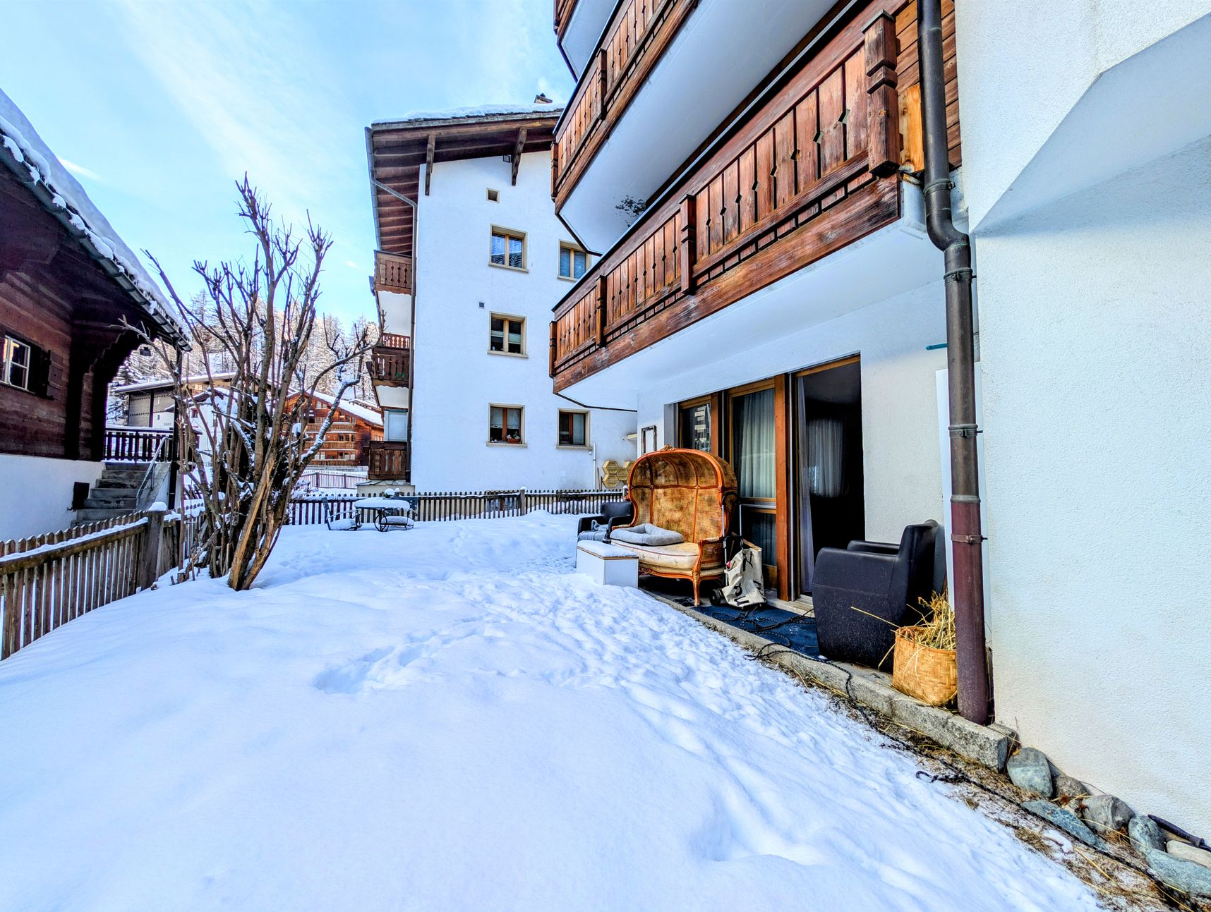 Schneebedeckter Innenhof eines alpinen Wohnhauses mit Balkon und Sitzplatz