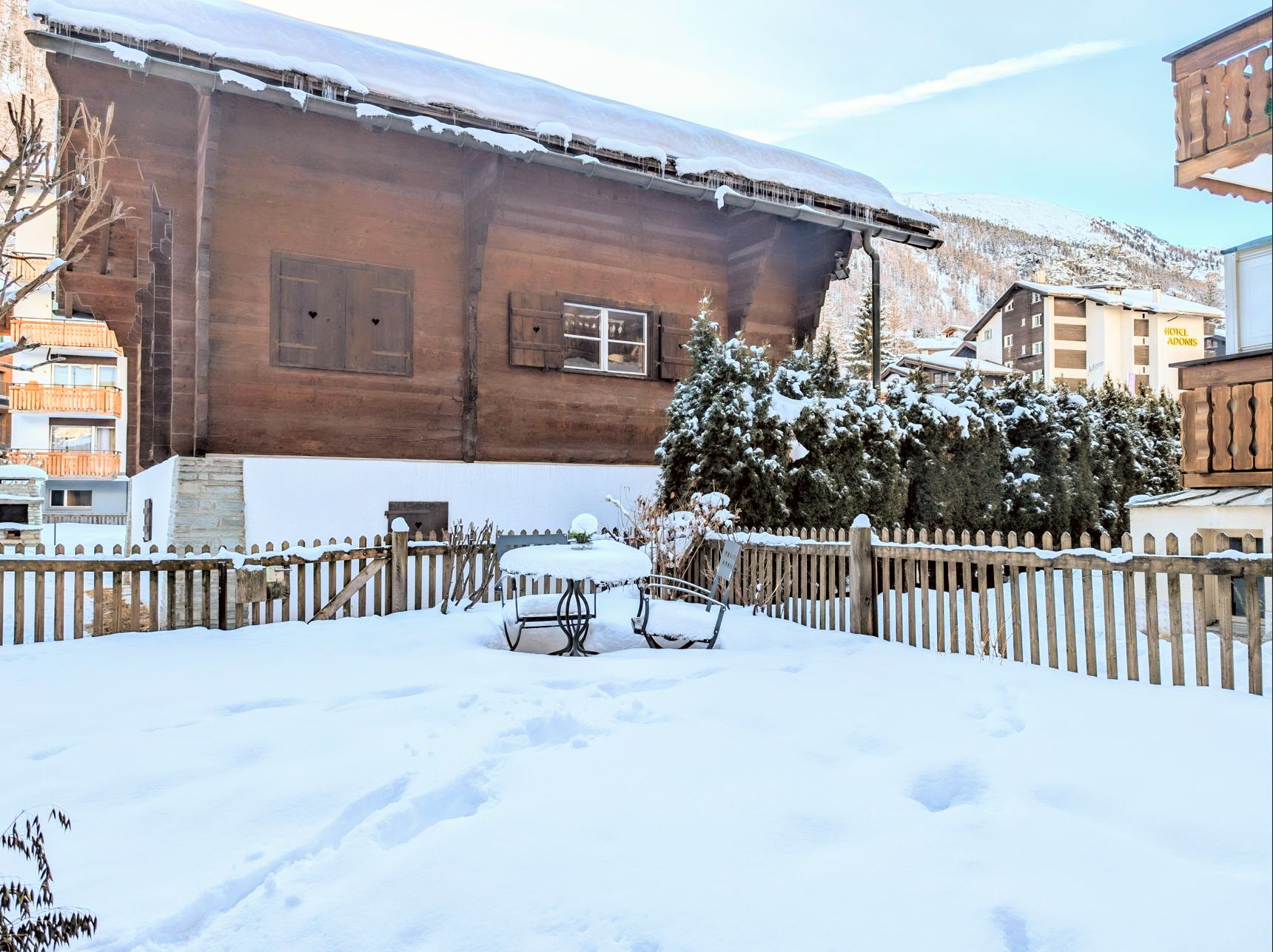 Verschneiter Garten mit alpinem Holzhaus