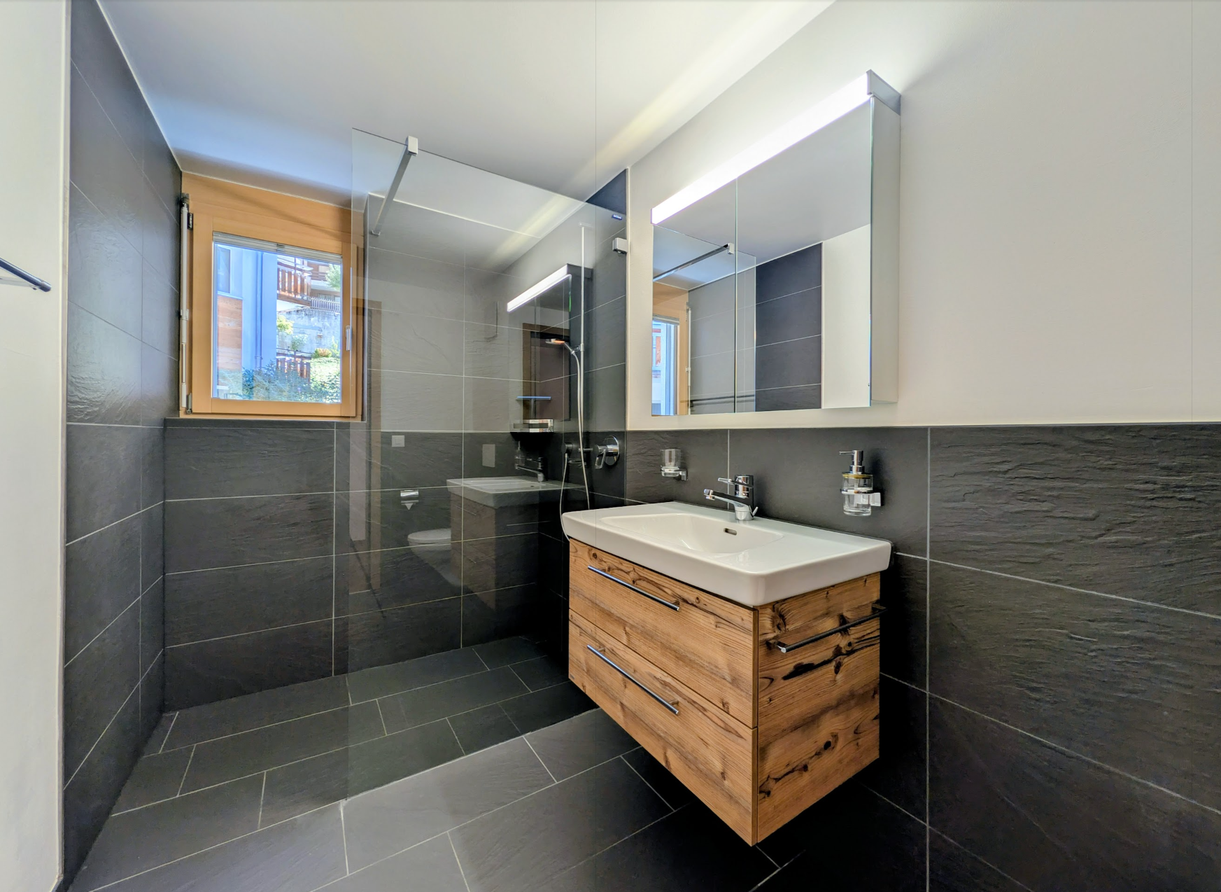 Modernes Badezimmer mit dunkler Natursteinoptik und Holzwaschtisch