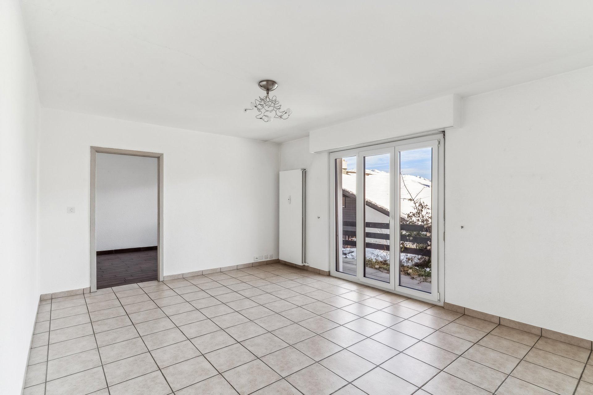 Leerer, heller Raum mit Fliesenboden und Balkonfenster