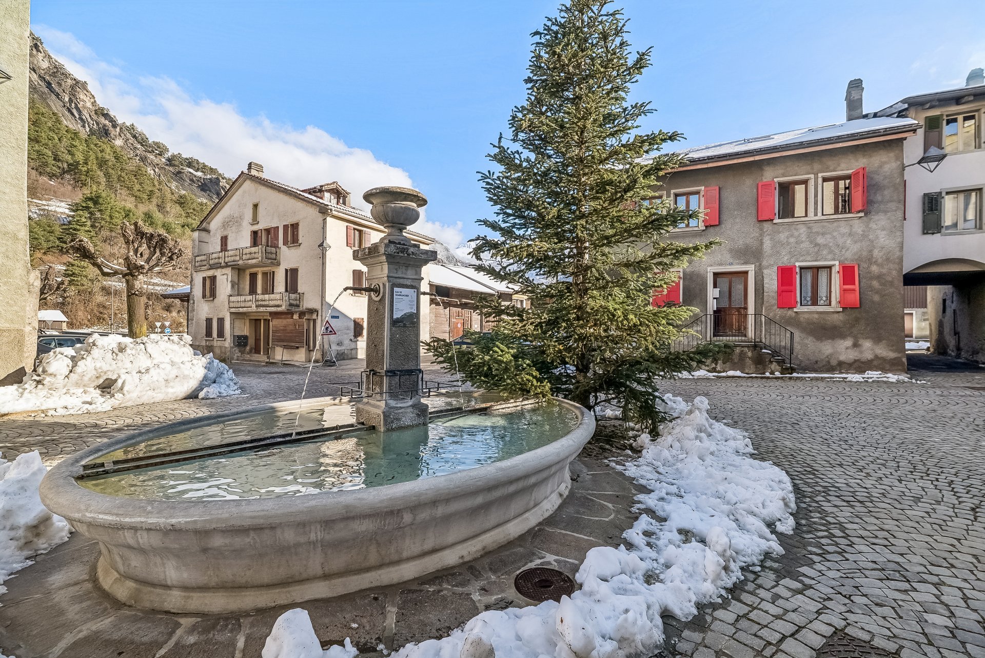 Dorfplatz mit Brunnen und Winterlandschaft