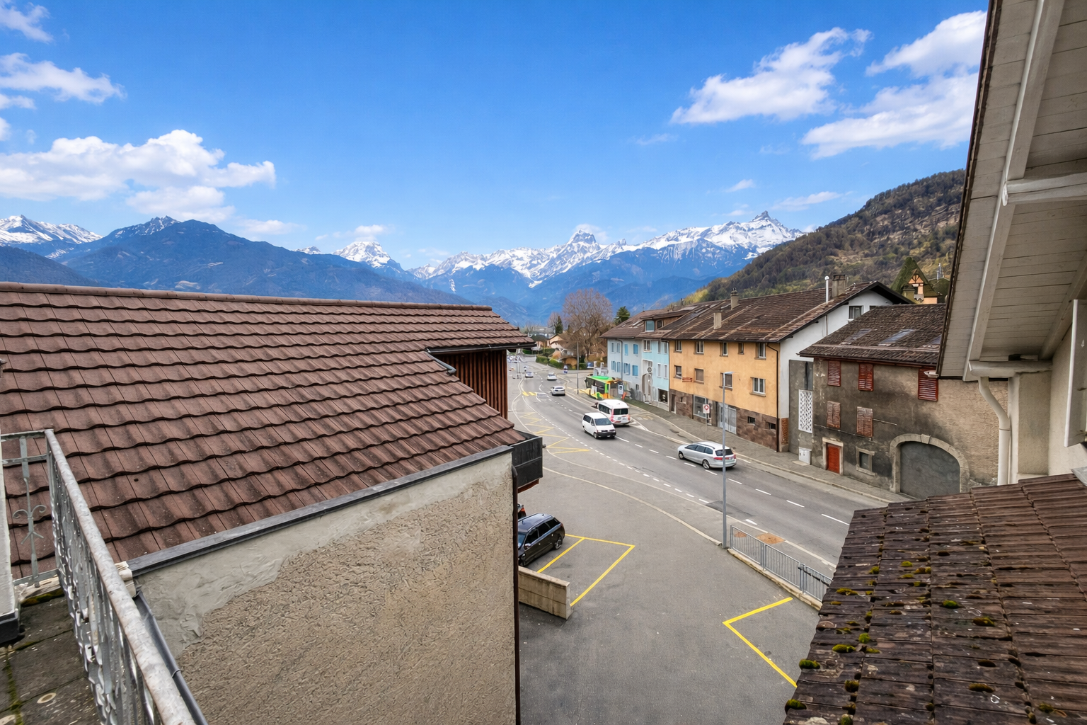 Blick von oben auf eine Straße mit Alpenpanorama