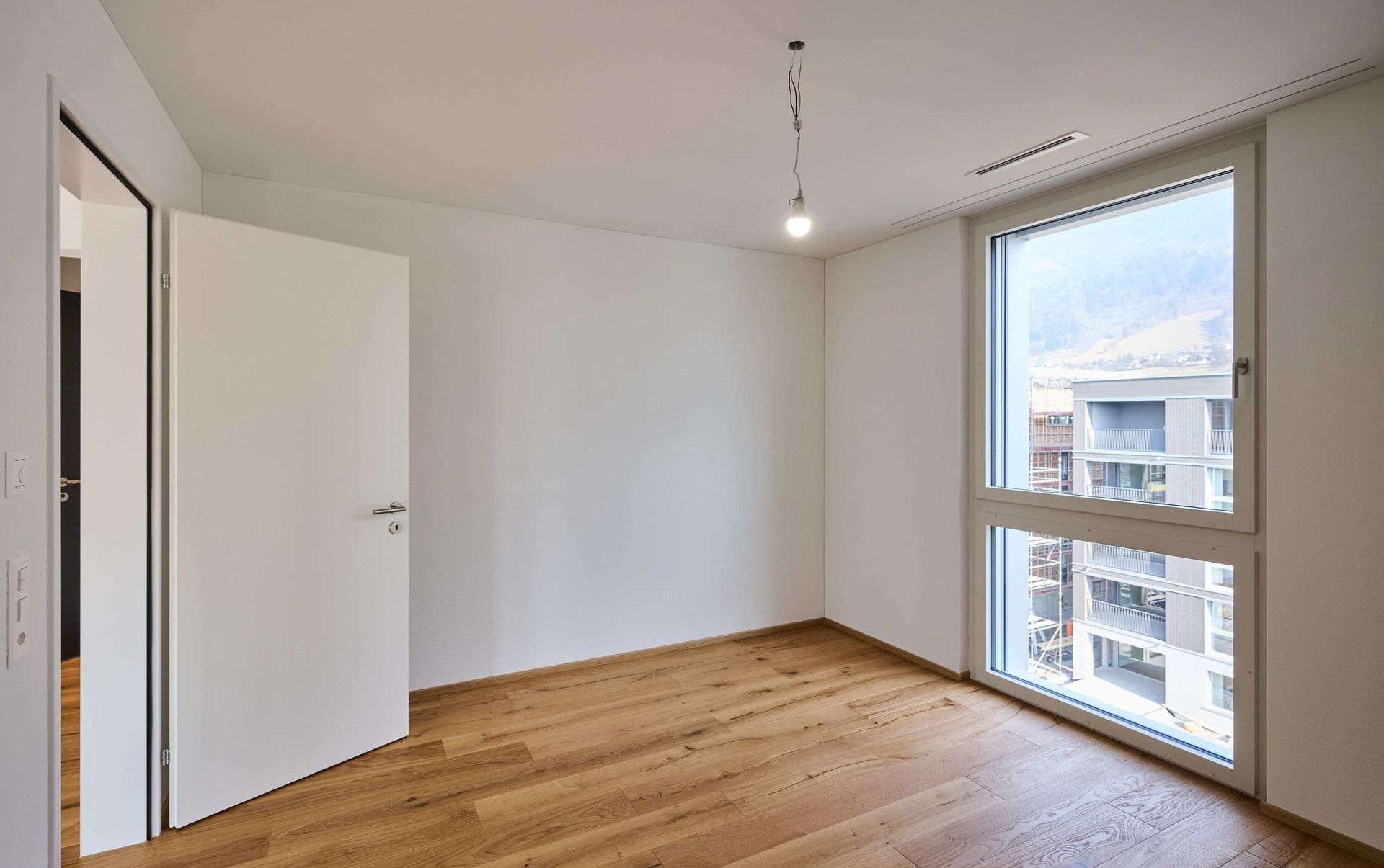 Leerer, heller Raum mit Holzfußboden und großem Fenster
