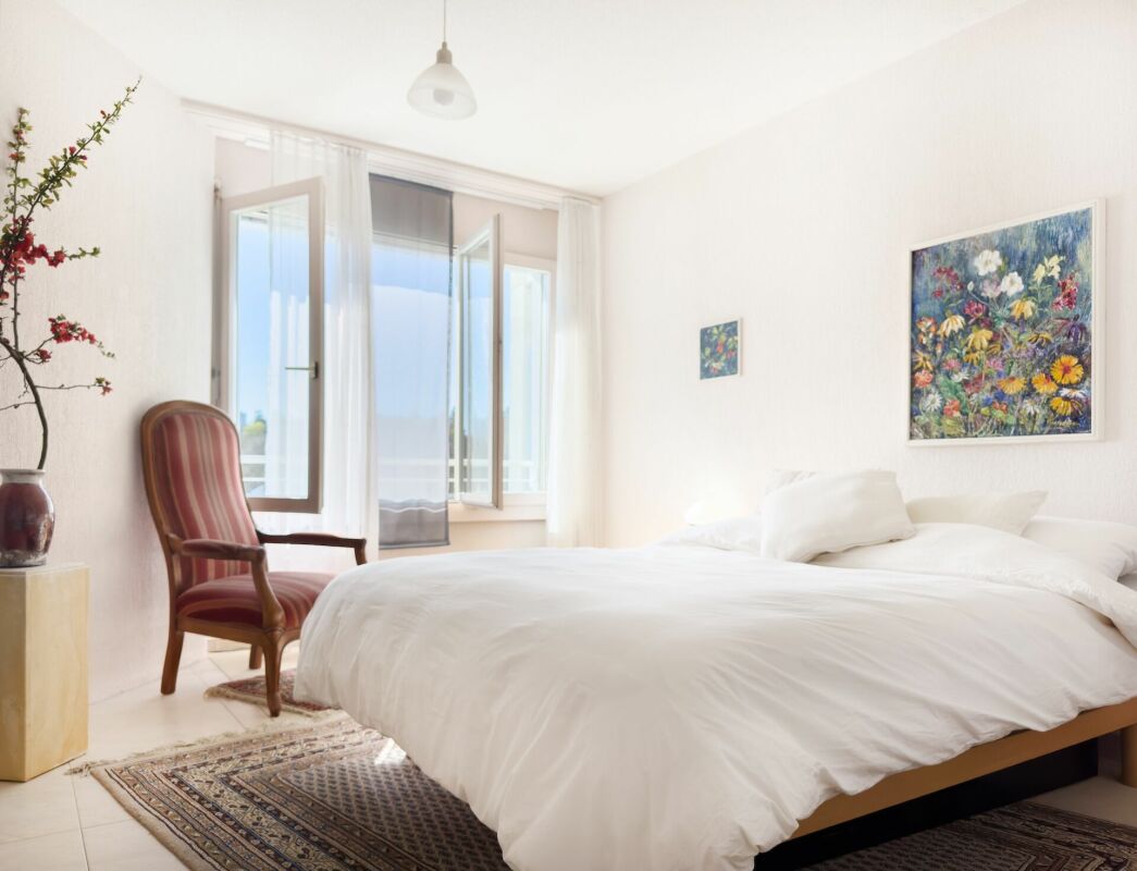 Helles Schlafzimmer mit geöffnetem Fenster und klassischer Sitzgelegenheit
