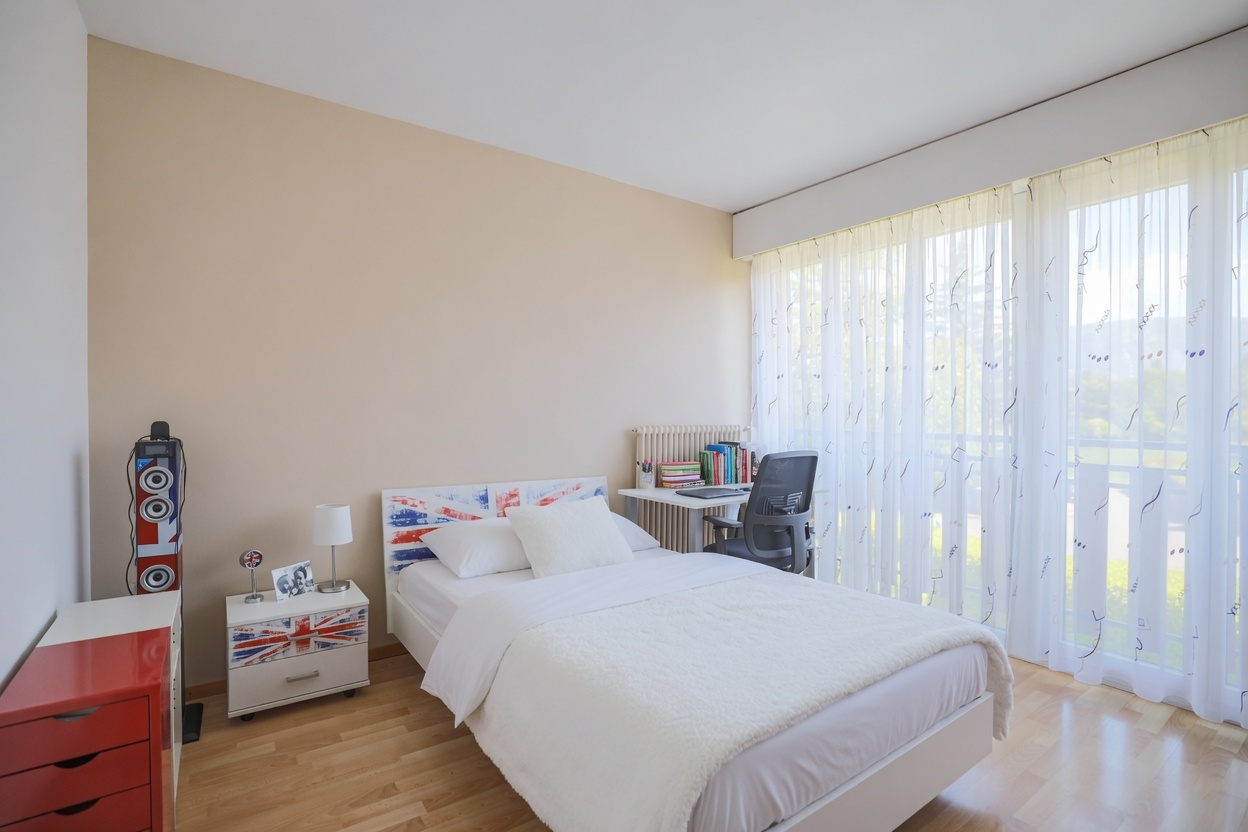 Helles Schlafzimmer mit großem Fenster und schlichtem Mobiliar