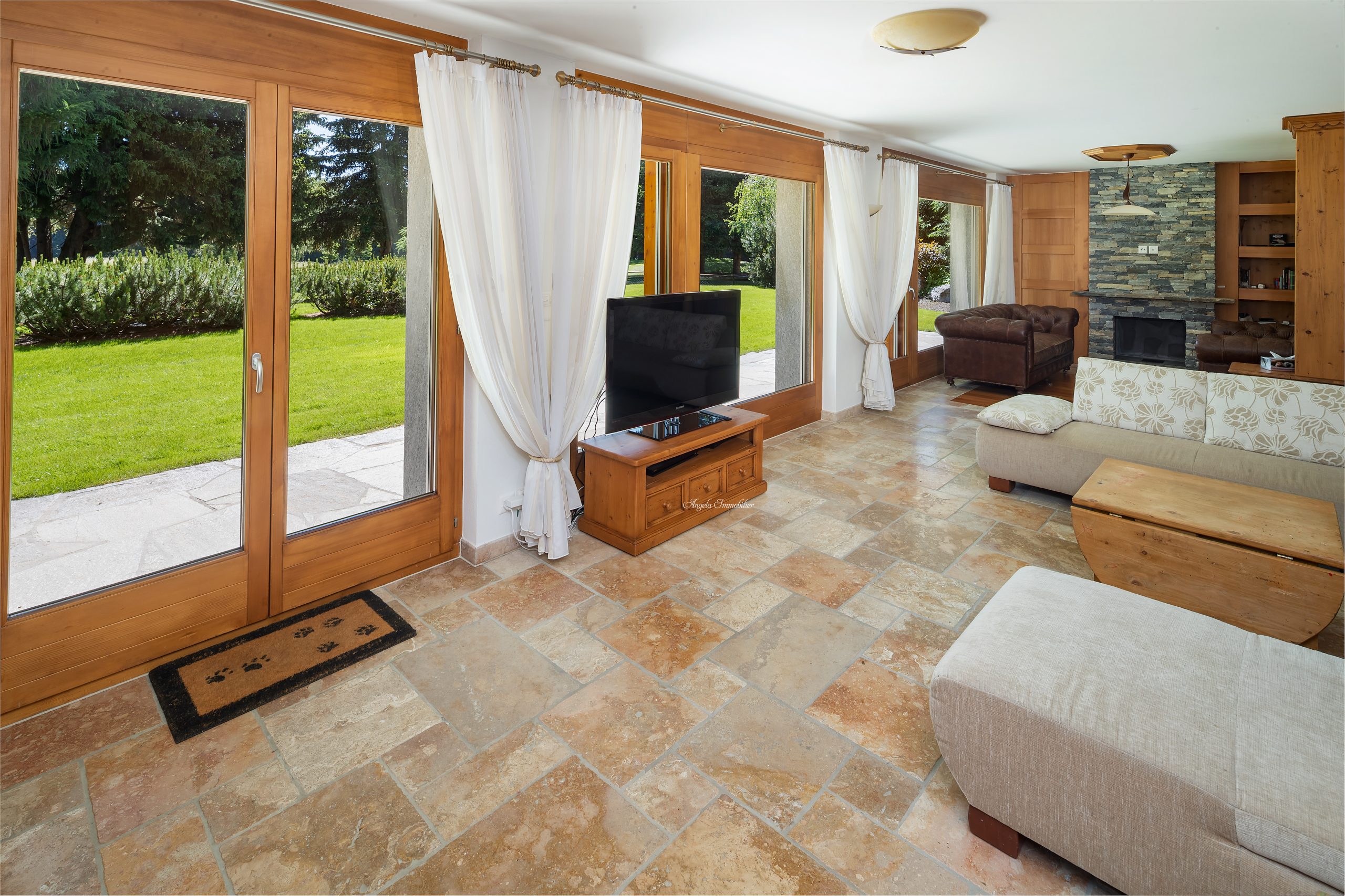 Helles Wohnzimmer mit großen Holzfenstern und Steinkamin