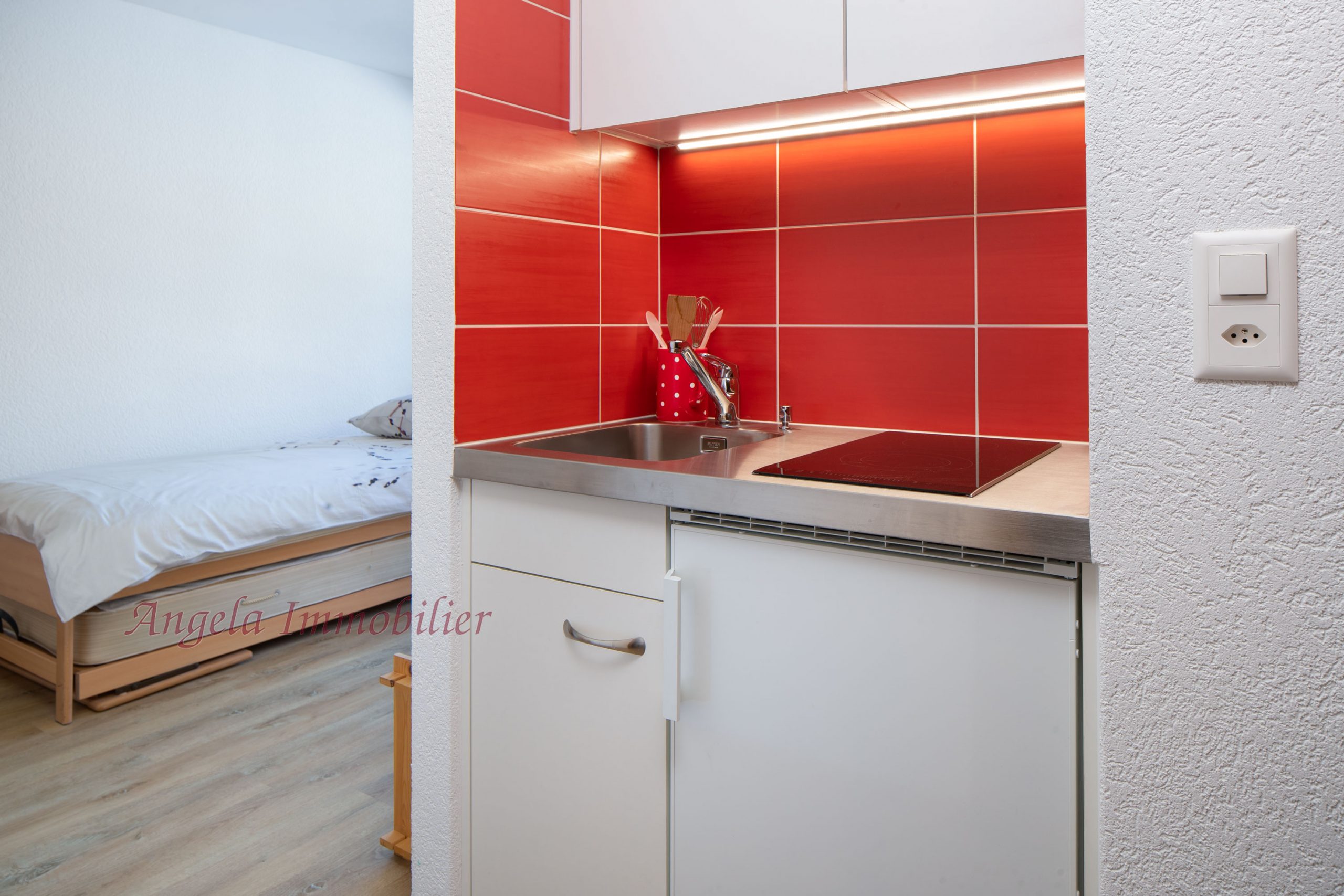 Kleine Küchenzeile mit roter Nischenverkleidung neben einem Schlafbereich