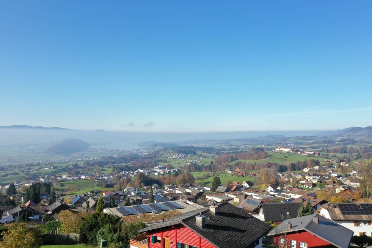 Panoramablick über eine Hügellandschaft mit Ortschaft und See in der Ferne