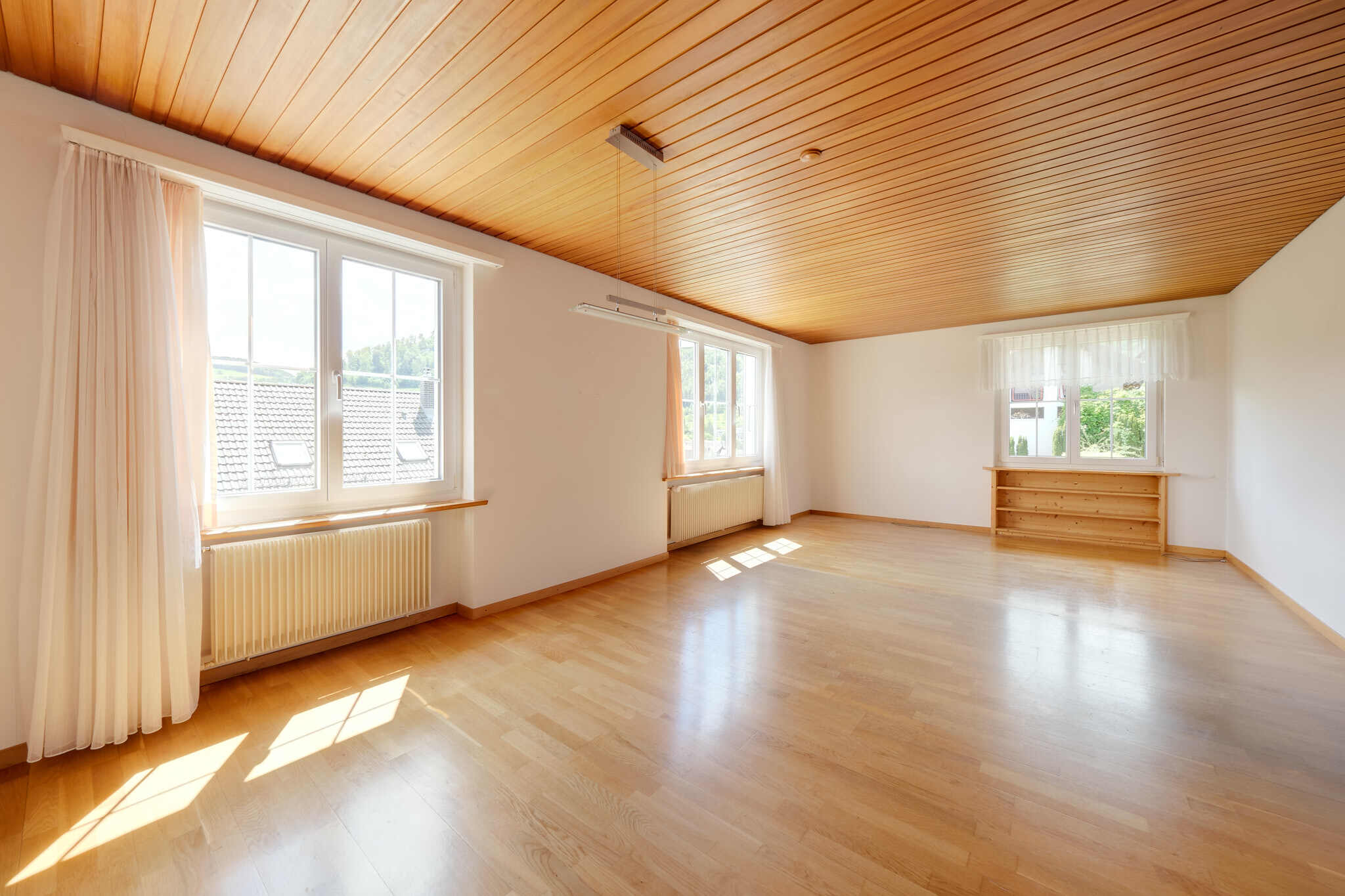 Heller leerer Wohnraum mit Holzdecke und Blick ins Grüne