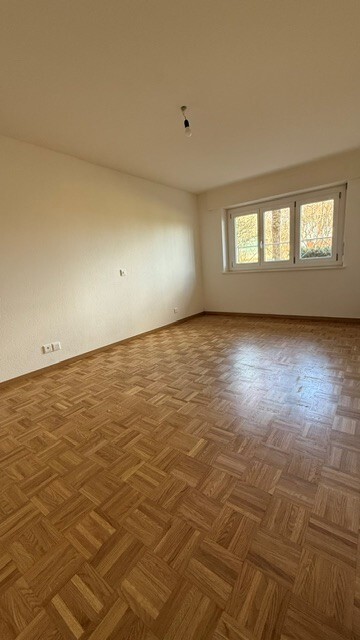 Leerer Wohnraum mit Parkettboden und Fenster