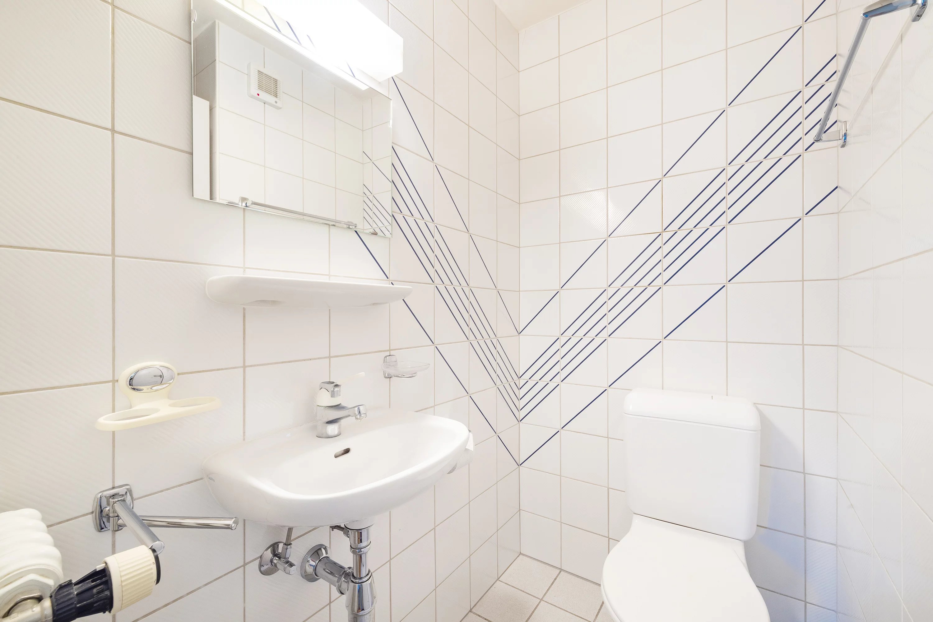 Kleines Gäste-WC mit weißer Fliesenverkleidung und blauem Linienmuster