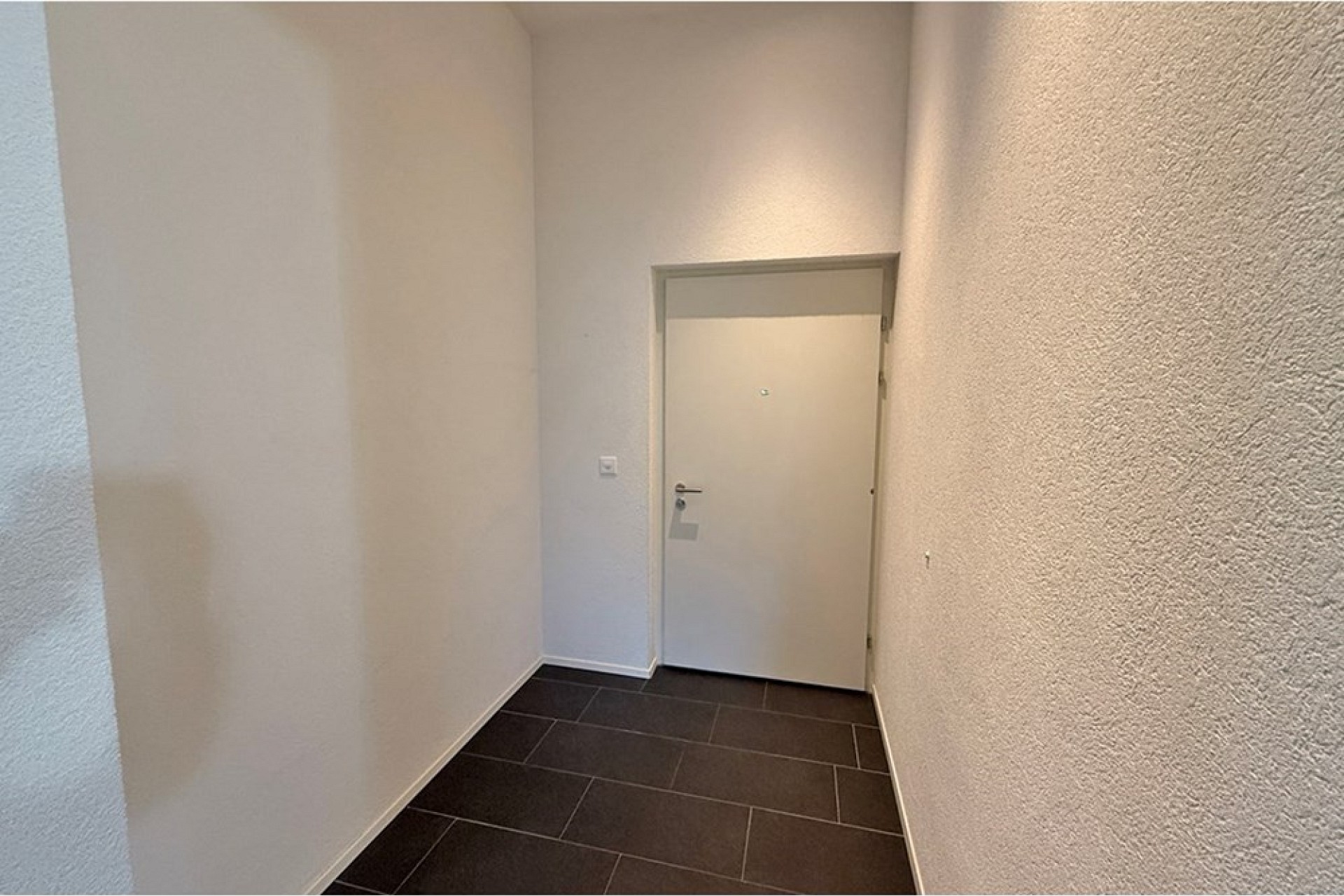 Schmaler Eingangsbereich mit Fliesenboden und weißer Tür