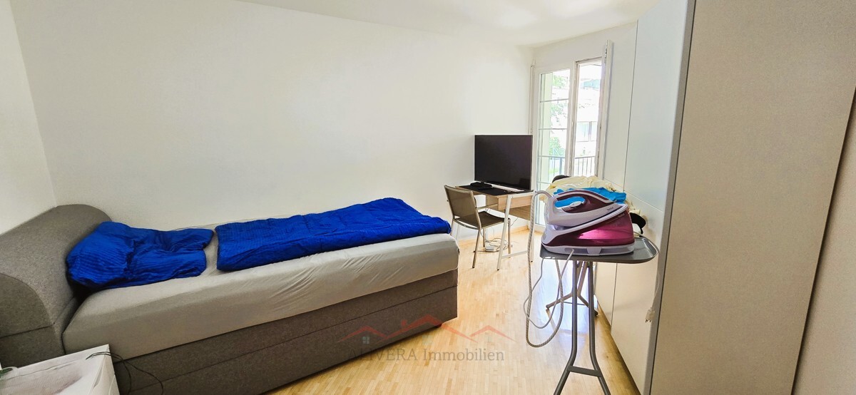 Schlichtes Schlafzimmer mit Bett und Arbeitsplatz am Fenster