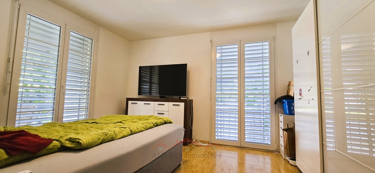 Helles Schlafzimmer mit großen Fenstern und Fernseher