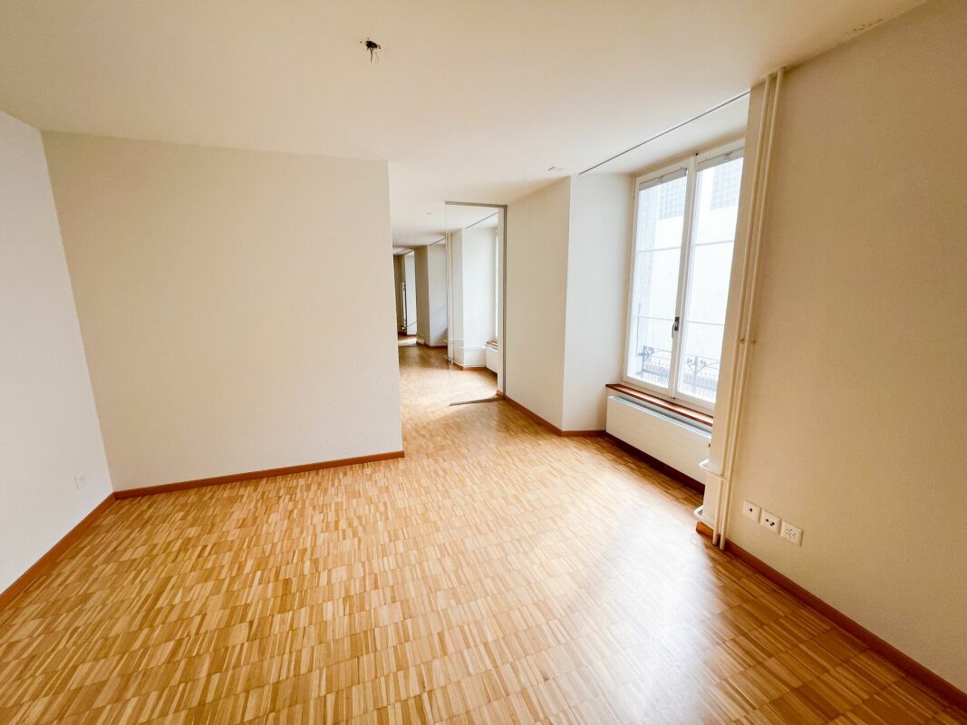 Heller leerer Wohnraum mit Parkett und großem Fenster