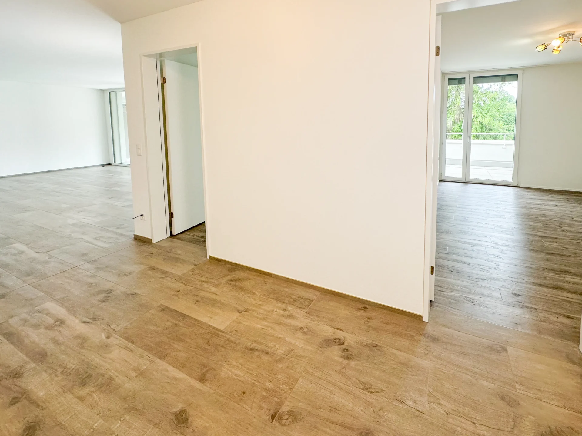 Helle leere Wohnfläche mit Holzboden und großen Fenstern