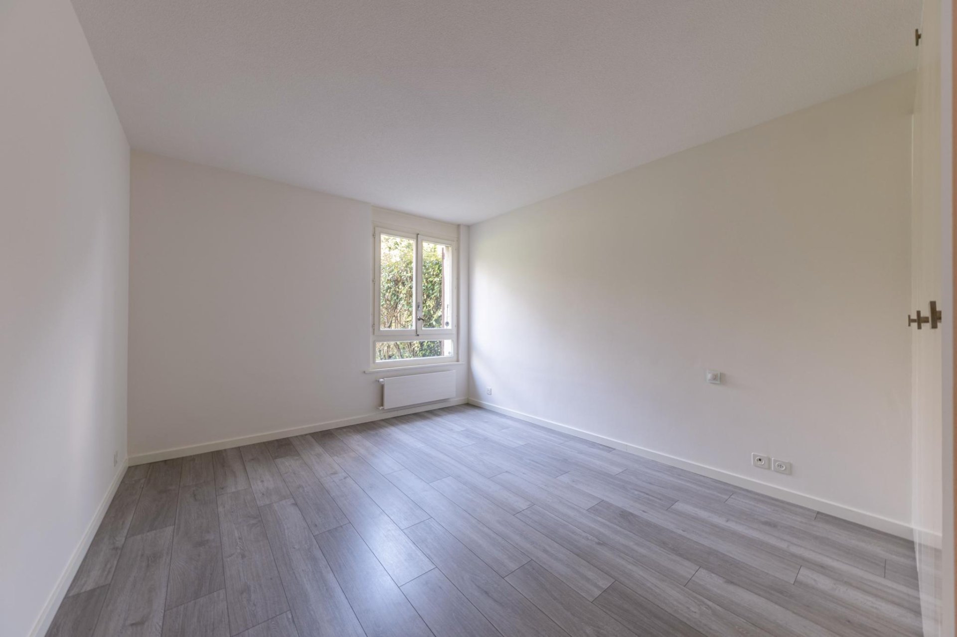 Heller leerer Raum mit Fenster und Holzoptikboden