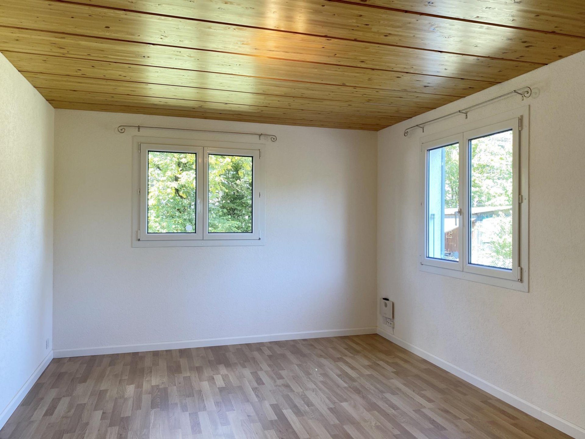 Heller leerer Raum mit Holzdecke und zwei Fenstern