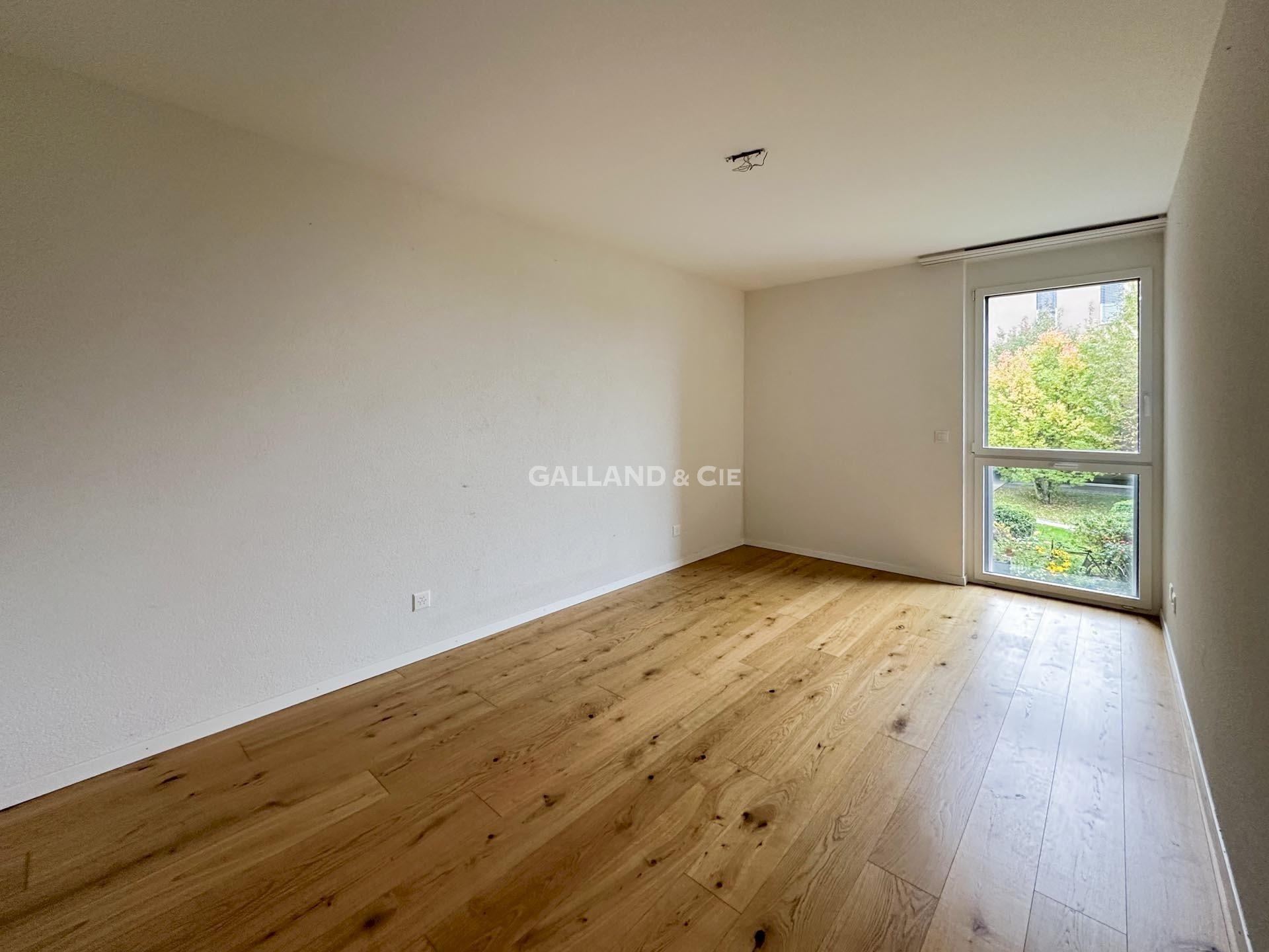 Helles, leeres Zimmer mit Holzfußboden und großem Fenster