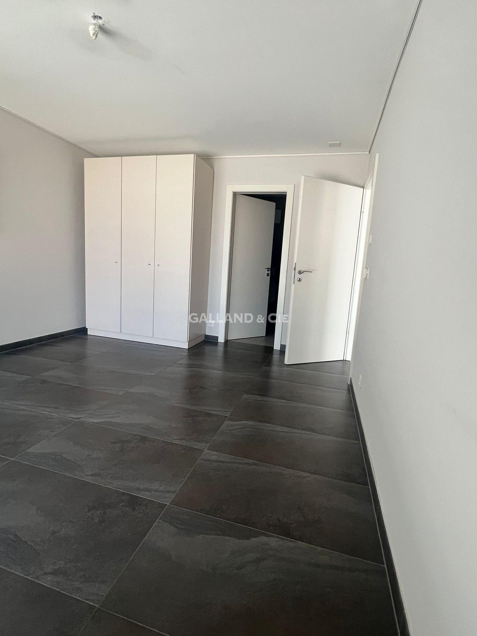 Helles, leeres Zimmer mit großformatigem dunklem Boden und Einbauschrank