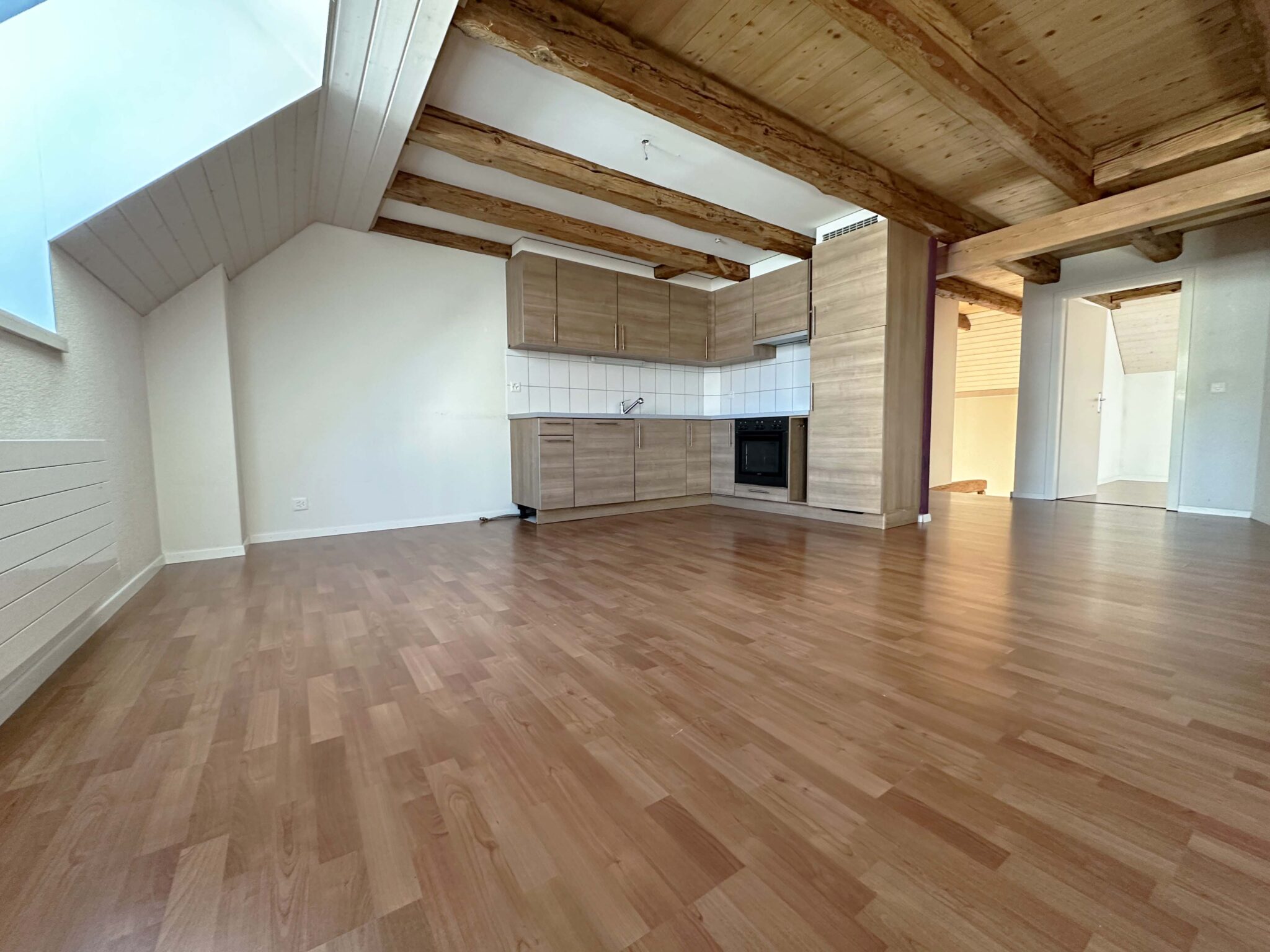 Offener Wohnraum mit Küchenzeile und sichtbaren Holzbalken