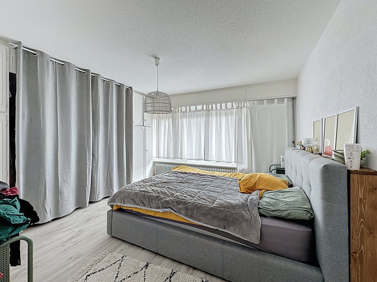 Helles Schlafzimmer mit grauem Polsterbett und Vorhängen
